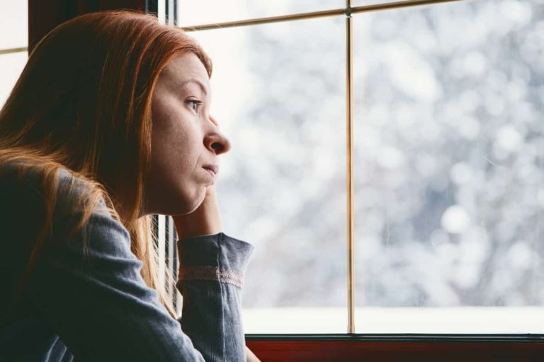 Frau sitzt am Fenster und klagt im Winter über Beschwerden, die auf eine depressive Verstimmung hindeuten